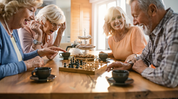 Group of happy seniors playing chess and having fun together at home.